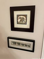Two framed elephant-themed wall art pieces hung on a wall, one square and one rectangular.