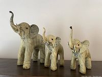 Three wooden elephant figurines arranged on a wooden surface against a plain background.