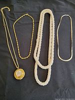 Four vintage costume jewelry necklaces displayed on black fabric, showing the full length and style of each necklace.