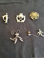 All 5 costume jewelry brooches displayed on a black background showing varied designs and finishes.