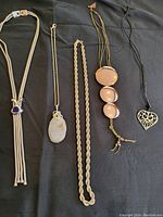 Five vintage costume jewelry necklaces displayed on black fabric, showing variety in styles and materials.