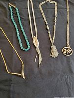 Full view of the five vintage costume jewelry necklaces laid out on black fabric, showing varied styles and colors.
