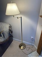 Floor lamp turned on, showing adjustable swing arm and white fabric shade, metal base and stand, cord on floor.