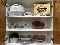 View of cupboard shelves with assorted casserole dishes and glass bakeware including Pyrex and CorningWare