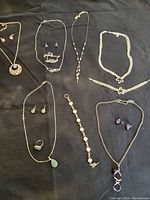 Photo showing an assortment of vintage costume jewelry sets on black fabric including matching necklaces, earrings, bracelets, and a ring with various colored stones and silver-tone metals.