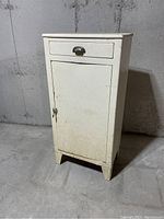 Front view of white metal kitchen or medical cabinet with drawer and door showing wear.
