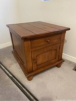 Front and side view showing the solid timber wood end table with drawer and cabinet door, on carpeted floor against wall.