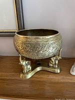 Side view showing the brass planter bowl with engraved floral pattern and the three brass elephant figures supporting the base.