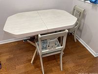 Photo showing the vintage kitchen table with two matching chairs positioned in a corner, light wood finish, angled edges on table top.