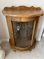 Front view of the wooden curio cabinet showing curved glass panels and top decorative wood backstop.