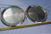 Two 12-inch round stainless steel griddles side by side with handles, showing overall condition and design.