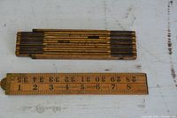 Two wooden folding measuring tapes folded flat showing wood grain and faded black measurement markings.