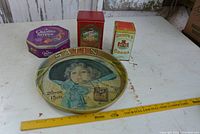 Overview of three colourful metal tins and vintage round tray on white surface with measuring ruler.