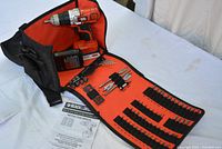 Black & Decker cordless drill in carrying case with bits and batteries, instruction manual visible on table.