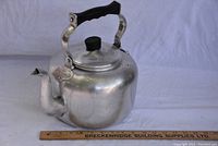 Full view of the aluminum kettle with wooden handle, showing body and spout dent.