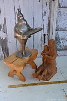 Three display items: metal Santa figure on circular base holding tray, small wooden stool, hand-carved wooden mother and child sculpture arranged together with measuring tape.