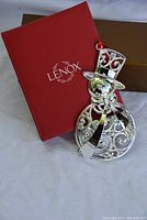 Photo of Lenox snowman ornament resting on original brown box with red Lenox-branded box lid leaning against it.