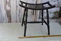 Side and front angle view of the black wooden bench showing curved seat slats, turned legs, and horizontal stretchers. A measuring stick placed on the floor shows approximate dimensions.