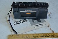 Front view of Panasonic RX-2700 portable radio cassette recorder with wrist strap, buttons, and speaker. The cassette compartment is visible with stereo branding and tuning scale above it.