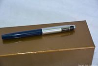 Side view of the Sheaffer pen laying on a brown box, showing blue barrel and silver cap with black top.