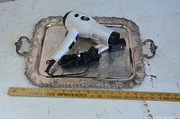 Silver metal tray with ornate edges and handles, ruler shows size approx 20x13 inches. T3 Bella hair dryer placed on the tray with power cord coiled.