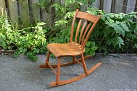 Full view image of the wooden rocking chair with natural wood finish and outdoor background showing the chair's size and construction.