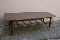 Front and side view of vintage coffee table showing brown finish, rectangular top, tapered legs, and slatted lower shelf.
