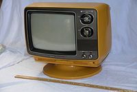 Front and right side view of mustard yellow Toshiba Blackstripe color television on swivel base with ruler