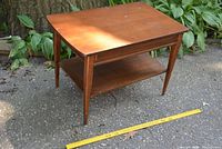 Photo showing full perspective of the vintage wood end table with two levels on an outdoor surface next to leaves and a yellow measuring stick used for size reference.