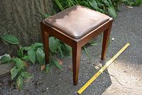 Side view of the vintage sewing stool showing rectangular wooden frame and brown removable cushion with measuring tape indicating size.