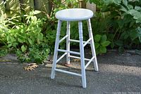 Full view of the white wooden stool showing its round seat, four turned legs, and horizontal support bars.