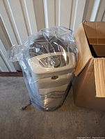 Air purifier wrapped in plastic next to open box showing protective styrofoam inserts.