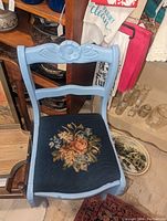 Blue wooden chair with carved floral design on backrest and embroidered seat upholstery