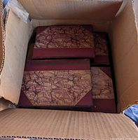 Photo showing the top view of a cardboard box filled with antique Cooper novels bound in maroon leather with marbled covers.
