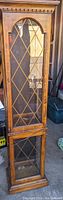 Full height view of the tall wooden display cabinet showing the diamond-patterned glass door and the top dentil molding detail.