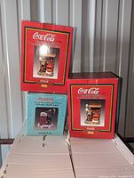 Three Coca-Cola limited edition Emmett Kelly collectible figurines in original boxes stacked showing their front and side views including box artwork and branding.