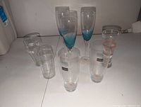 Top-down and angled photos of 8 assorted drinking glasses including champagne flutes and Coca-Cola branded glasses.