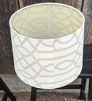 Beige and cream abstract pattern contemporary lamp shade with cylindrical shape and metal frame inside, shown on wooden surface.