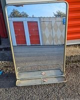 Front view of rectangular mirror showing gold-tone metal frame and bottom shelf with raised bars.