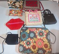 Overview photo of seven assorted purses and handbags arranged on the floor - shows variety of colors, sizes and styles