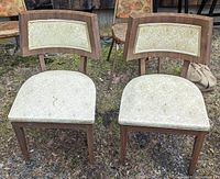 Pair of Mid-Century Modern chairs shown from the front, seated outdoors on gravel. Both chairs have wooden frames and light floral fabric upholstery on seats and backs.
