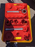 Open red and yellow hard plastic case showing pipe threading tools including dies and handles.