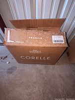 Open cardboard box showing Corelle packaging labeled fragile
