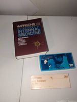 Vintage 12th edition Harrison's Principles of Internal Medicine book with a burgundy cover, alongside a blue boxed Littmann stethoscope and white boxed Littmann ECG Trimmer No. 205.