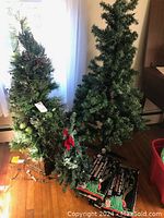 Three artificial Christmas trees arranged inside a room, showing varying heights and dense green foliage with some tags attached.