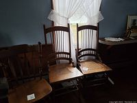 Two antique wooden dining chairs with cane seats and curved backs side by side near a window.