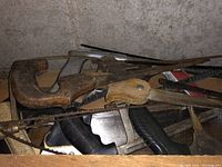 Various hand saws with wooden and plastic handles, saw blades, and a plastic case for a circular saw shown piled in a workbench drawer.
