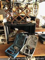 Photo showing two electric drills in blue and white plastic cases, a bottle rack on a rolling cart, and some boxed items.