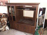 Front view of wooden entertainment center showing glass doors, upper shelf, and bottom storage