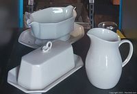 White glazed ceramic pitcher, ceramic covered butter dish, and plates on a shelf